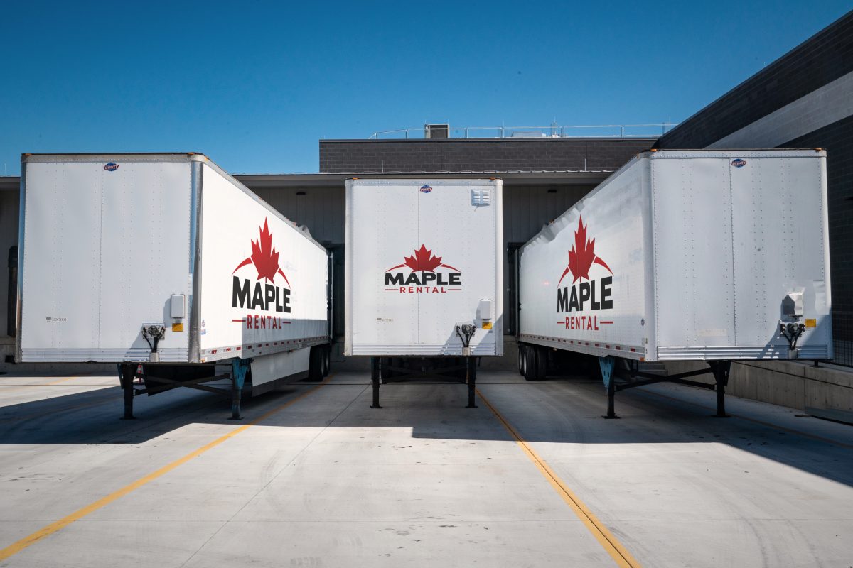 Three white Maple Rental storage trailers parked at a business's loading docks
